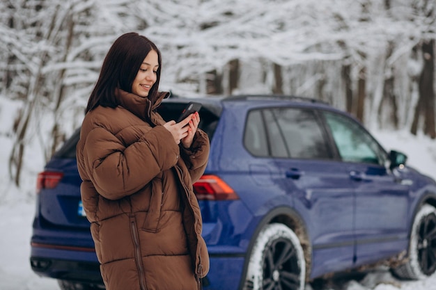 Frau mit Telefon steht an ihrem Auto im Winterwald