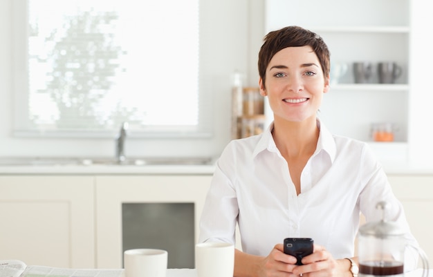 Frau mit Telefon und Kaffee, die zur Kamera schauen