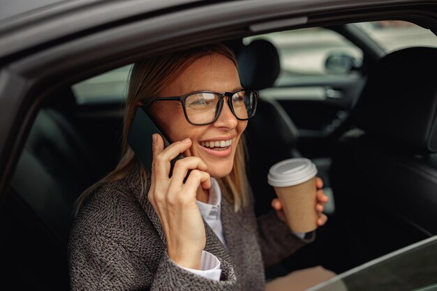 Frau mit telefonierendem Kaffee, die auf dem Rücksitz des Taxis sitzt und auf dem Weg zum Fenster auf das Fenster blickt