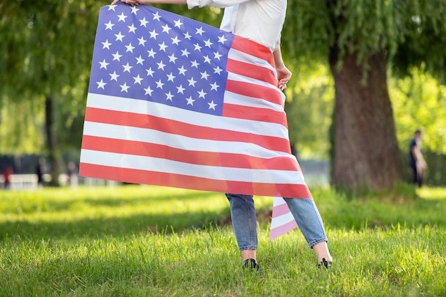 Frau mit USA-Nationalflagge um ihre Taille, die draußen im Sommerpark steht