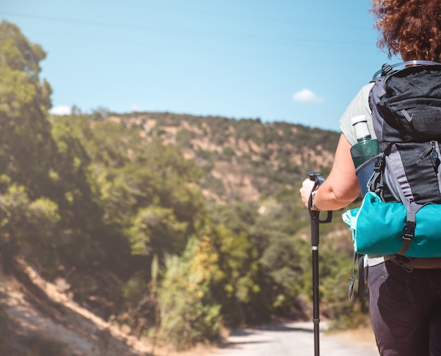 Frau mit Wanderausrüstung, die in der grünen Berglandschaft an einem sonnigen Tag geht