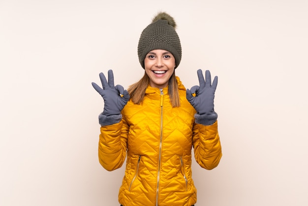 Frau mit Wintermütze über isolierter Wand, die ein OK-Zeichen mit den Fingern zeigt