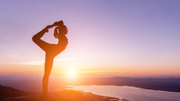 Frau mit Yoga-Haltung auf dem Berg bei Sonnenuntergang