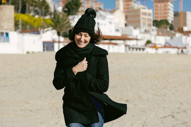 Frau mittleren Alters, die an einem sonnigen Wintertag glücklich am Strand entlang läuft