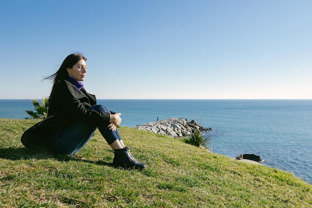 Frau mittleren Alters, die an einem Wintertag vor dem Meer meditiert