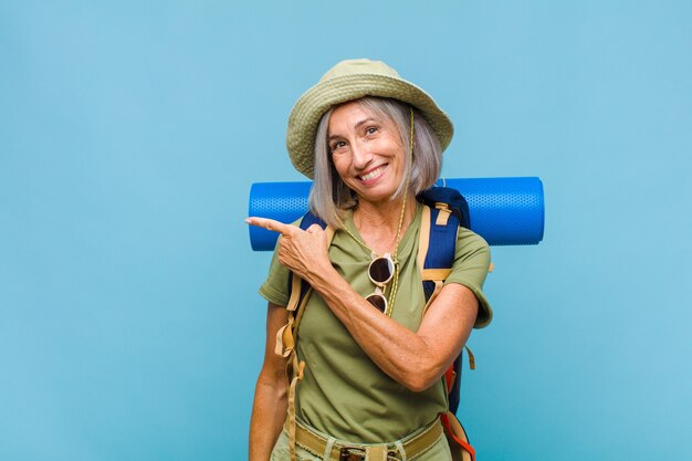 Frau mittleren Alters, die aufgeregt und überrascht aussieht und zur Seite und nach oben zeigt, um Raum zu kopieren