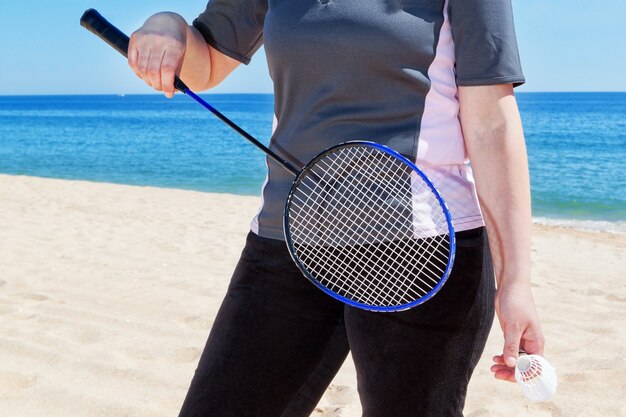 Frau mittleren Alters, die Badminton am Strand spielt. Sommer.