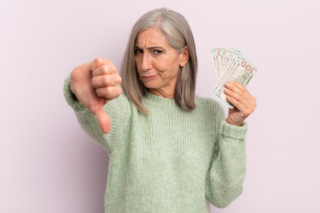 Frau mittleren Alters, die das Gefühl hat, Daumen nach unten zu zeigen, Dollar-Banknoten-Konzept