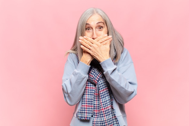 Frau mittleren Alters, die den Mund mit Händen mit einem schockierten, überraschten Ausdruck bedeckt, ein Geheimnis bewahrt oder Hoppla sagt