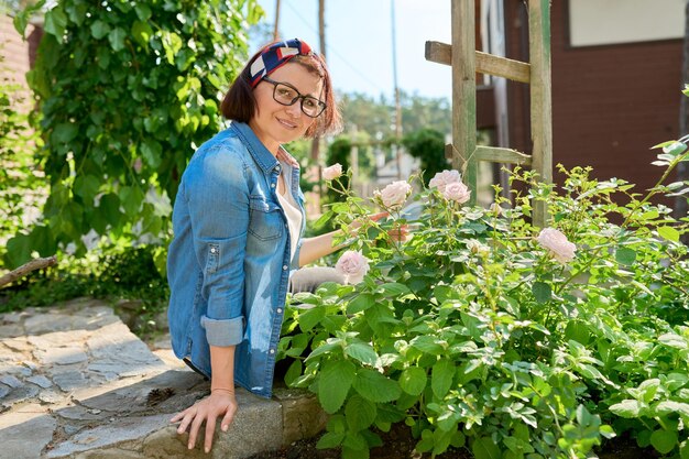 Foto frau mittleren alters, die die schönheit der rosenbusch-frühlingsnatur genießt