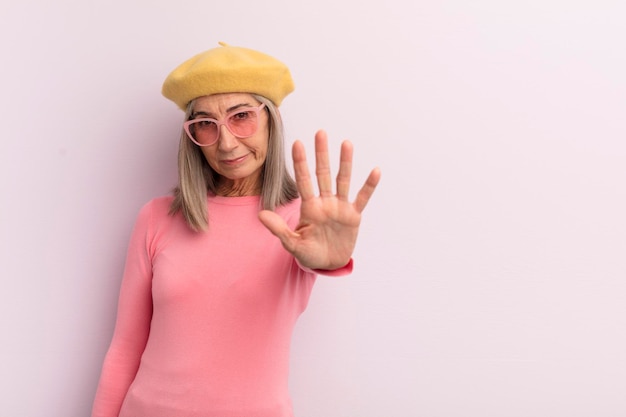 Frau mittleren Alters, die ernsthaft aussieht und eine offene Handfläche zeigt, die eine Stoppgeste macht