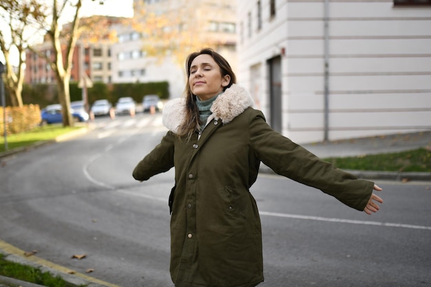 Frau mittleren Alters, die im Winter abends vor der Kälte gebündelt ist und mit offenen Armen die kalte und frische Abendluft einatmet, Zustimmung der Freiheit