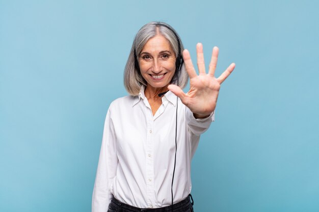 Frau mittleren Alters, die lächelt und freundlich aussieht, die Nummer fünf oder fünf mit der Hand nach vorne zeigt und herunterzählt. Telemarketing-Konzept