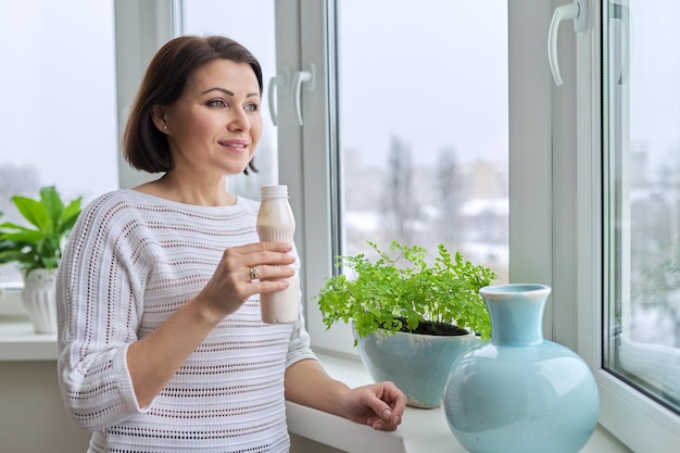 Frau mittleren Alters, die Milchproduktjoghurtmilch in der Flasche trinkt