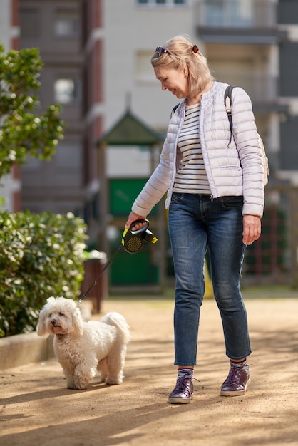 Frau mittleren Alters, die mit flauschigem weißem Hund in der Sommerstadt geht.