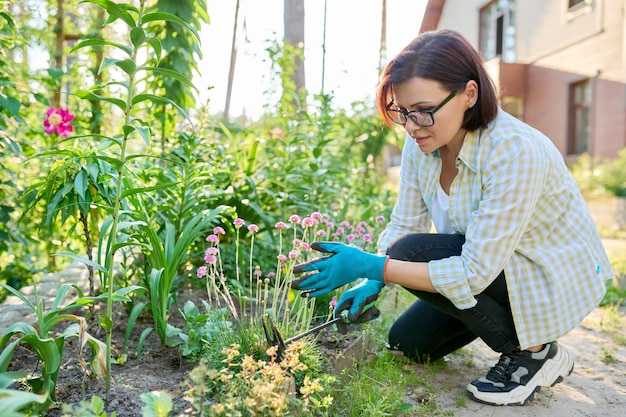 Frau mittleren Alters, die mit Gartengeräten im Blumenbeet arbeitet