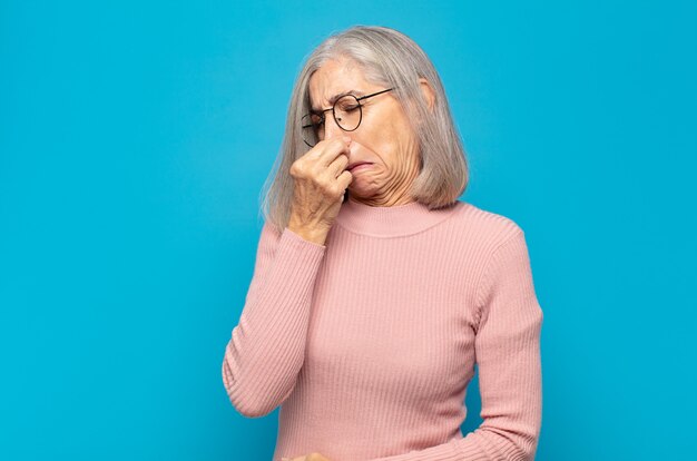 Frau mittleren Alters, die sich angewidert fühlt und die Nase hält, um einen üblen und unangenehmen Gestank zu vermeiden