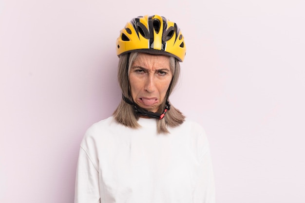 Frau mittleren Alters, die sich angewidert und gereizt fühlt und das Fahrradhelmkonzept mit der Zunge herausstreckt