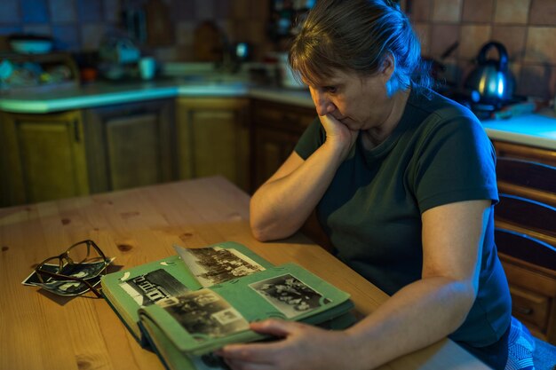 Frau mittleren Alters, die sich das Familienfotoalbum anschaut Nostalgie Traurigkeit Erinnerungen an das Konzept des mittleren Alters