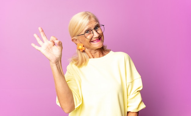 Frau mittleren Alters, die sich erfolgreich und zufrieden fühlt, mit weit geöffnetem Mund lächelt und mit der Hand ein gutes Zeichen macht