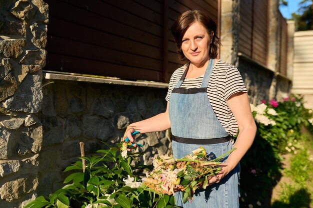 Frau mittleren Alters, die sich im Hinterhof mit Pruner um gelben Pfingstrosenstrauch kümmert