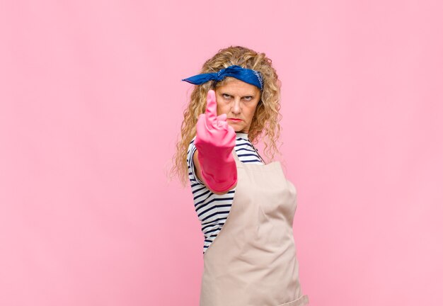 Foto frau mittleren alters, die sich wütend, verärgert, rebellisch und aggressiv fühlt, den mittelfinger umdreht und das konzept der haushälterin bekämpft