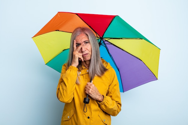 Frau mittleren Alters graue Haare, die sich nach einem ermüdenden Gefühl gelangweilt, frustriert und schläfrig fühlen. Regenschirm und Regenkonzept