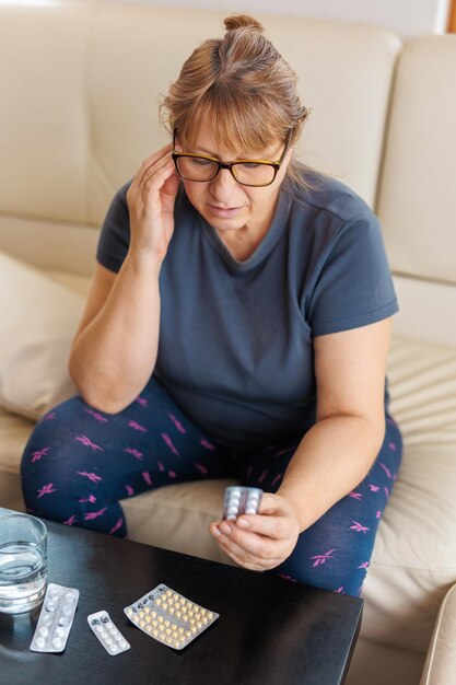 Frau mittleren Alters hält eine Blisterpackung mit Pillen und liest medizinische Anweisungen auf der Couch