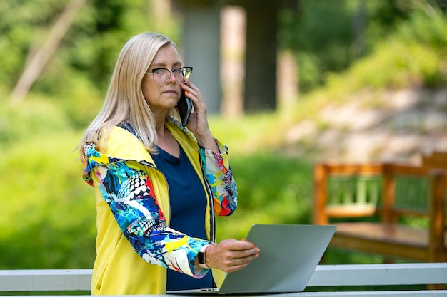 Frau mittleren Alters im Garten, die von zu Hause aus mit Laptop arbeitet und telefoniert