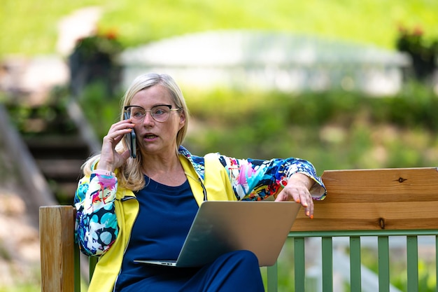 Frau mittleren Alters im Garten, die von zu Hause aus mit Laptop arbeitet und telefoniert