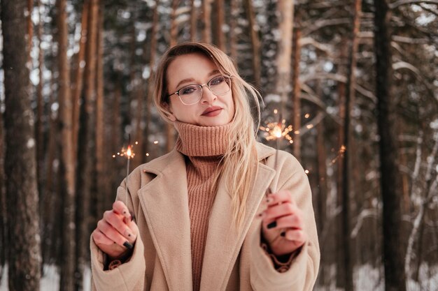 Frau mittleren Alters im Mantel steht im Winterwald mit Wunderkerze in der Hand im Freien