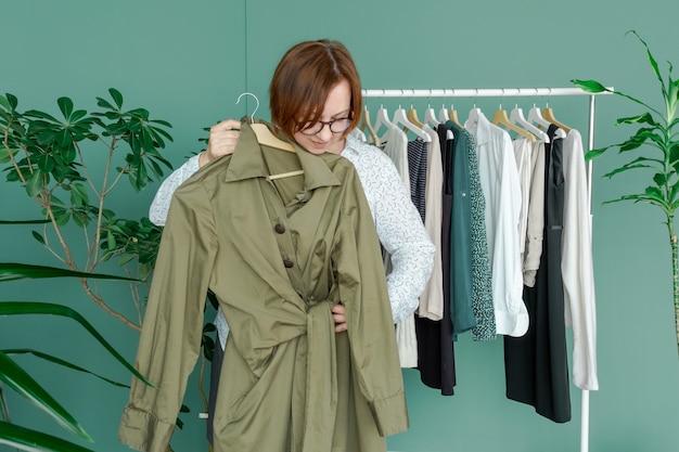 Frau mittleren Alters macht Einkaufen und betrachtet das neue Kleid in der Nähe des Regals mit Kleidung.