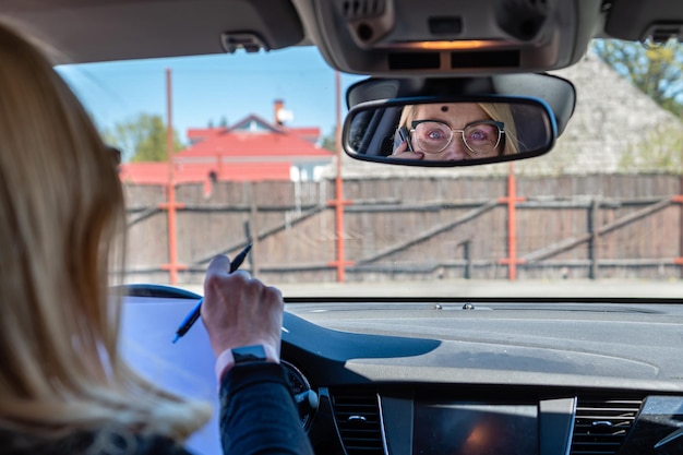 Foto frau mittleren alters mit brille im auto arbeitet mit dokumenten und spricht im telefon rückwärts