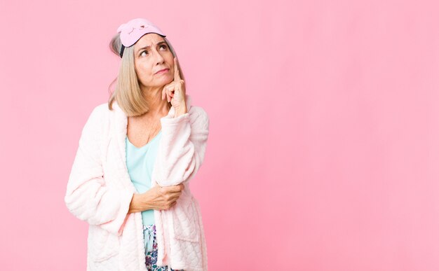 Frau mittleren Alters mit einem konzentrierten Blick, der sich mit einem zweifelhaften Ausdruck wundert und nach oben und zur Seite schaut. Nachtanzug-Konzept