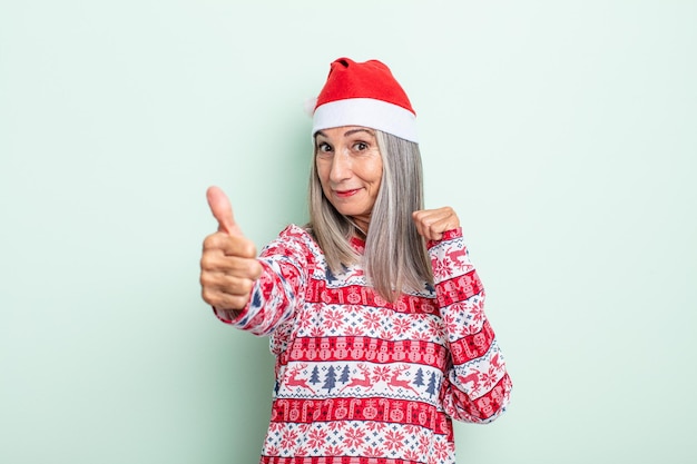 Frau mittleren Alters mit grauem Haar, die stolz ist und positiv mit Daumen nach oben lächelt. Weihnachtskonzept