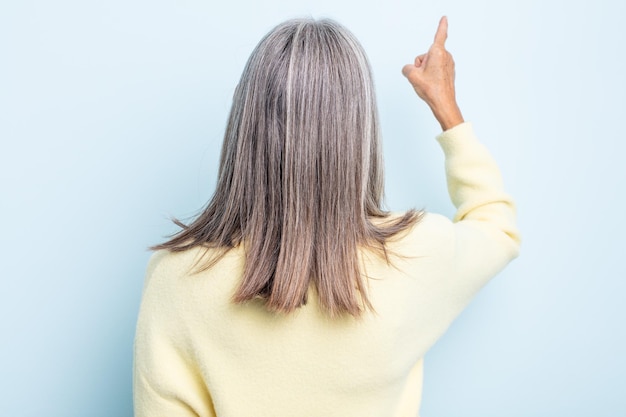 Frau mittleren Alters mit grauen Haaren, die auf dem Kopierraum steht und auf ein Objekt zeigt, Rückansicht