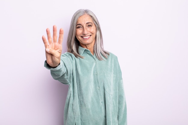 Frau mittleren Alters mit grauen Haaren, die lächelt und freundlich aussieht, die Nummer vier oder vier mit der Hand nach vorne zeigt und herunterzählt