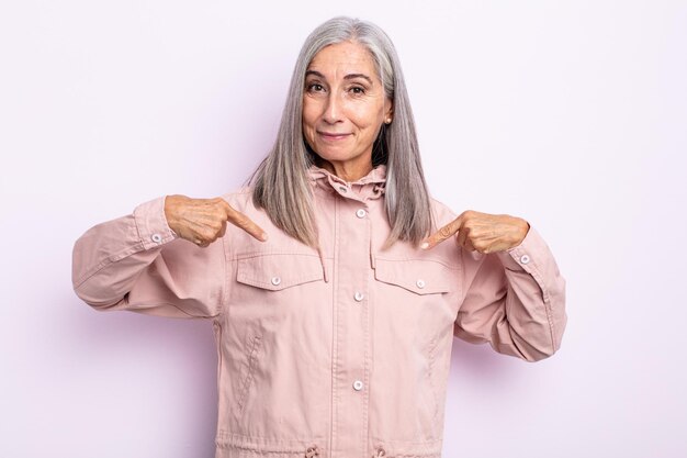 Frau mittleren Alters mit grauen Haaren, die stolz, positiv und lässig aussieht und mit beiden Händen auf die Brust zeigt