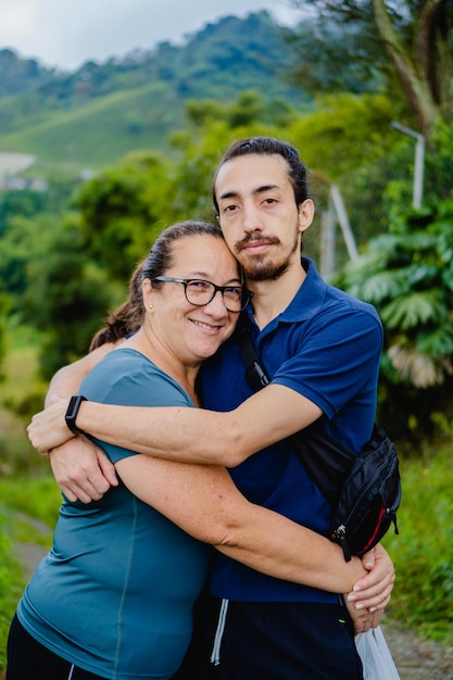 Frau mittleren Alters mit ihrem Sohn des jungen Mannes, der sich in der Natur umarmt und das vertikale Foto der Kamera anschaut