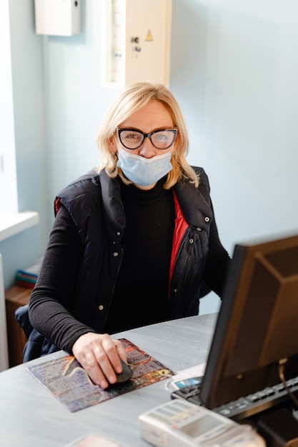 Frau mittleren Alters mit medizinischer Maske, die mit PC-Computer arbeitet. Kleinunternehmer in Quarantäne