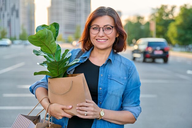 Frau mittleren Alters mit Papiereinkaufstüten mit Kaufpflanze, die in die Kamera schaut
