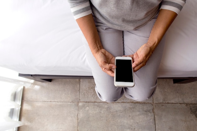 Frau mittleren Alters mit Smartphone im Bett, Ansicht von oben.