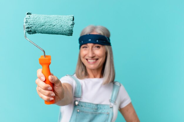 Frau mittleren Alters mit weißen Haaren, die eine Wand malt