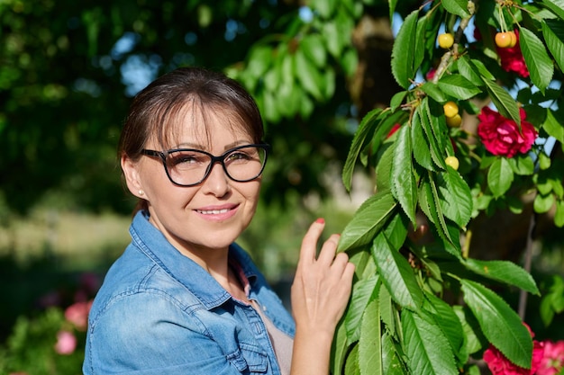 Frau mittleren Alters pflückt gelbe Kirschen im Garten. Köstlicher reifer, gesunder Vitamin-Sommerobstgarten der Saison mit Obstbäumen, natürliches Bio-Lebensmittelkonzept