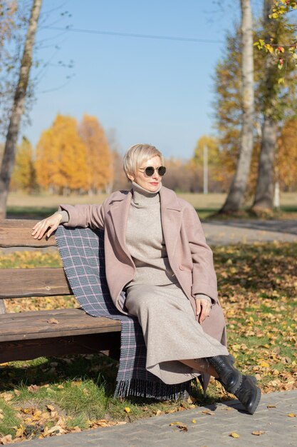 Frau mittleren Alters sitzt im Herbst auf einer Parkbank. Foto in hoher Qualität