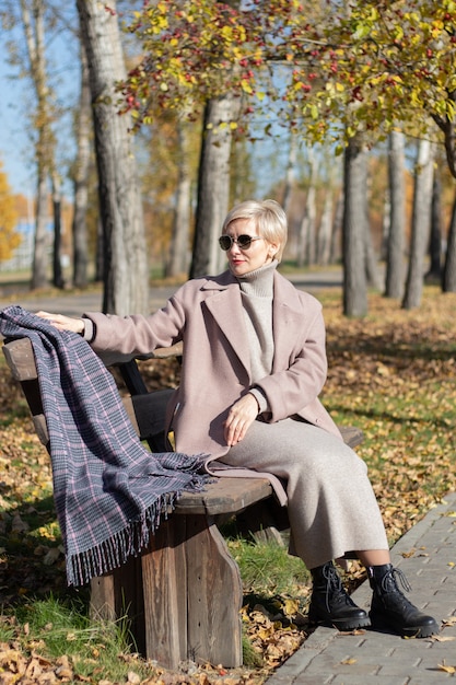 Frau mittleren Alters sitzt im Herbst auf einer Parkbank. Foto in hoher Qualität