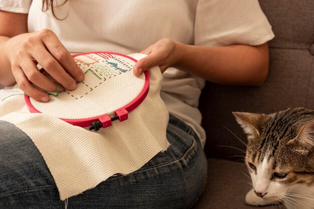 Frau näht Kreuzstich mit ihren Katzen auf dem Sofa zu Hause