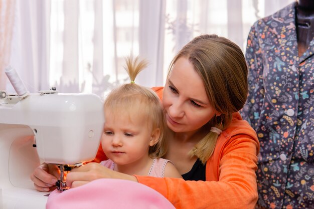 Frau näht zu Hause und zeigt ihrer kleinen Tochter ihre Arbeit