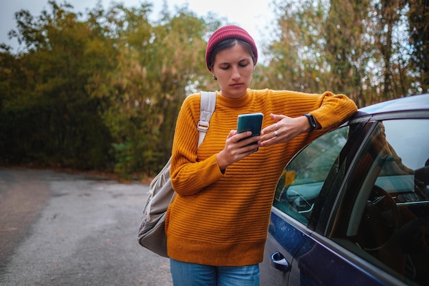 Frau neben einem Auto und Blick auf Smartphone