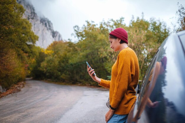 Frau neben einem Auto und Blick auf Smartphone